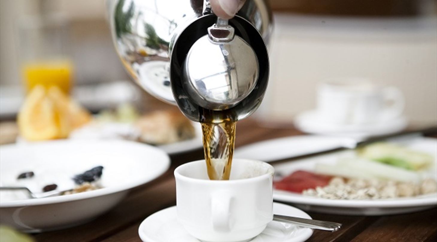 Billedet viser en kop kaffe på et bord med morgenmad